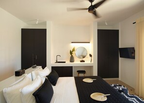 A modern bedroom with a bed, bedside tables, a vanity with a mirror, and a ceiling fan. - Absolute Paradise Santorini- Adults Only (Santorini)