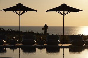 A poolside area with lounge chairs and umbrellas, overlooking the ocean at sunset. - Absolute Paradise Santorini- Adults Only (Santorini)