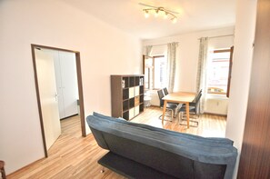 A compact living space with a sofa, a dining table with chairs, a bookshelf, and a door leading to another room.