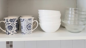 A shelf with clear glassware, white bowls, and patterned mugs. - Apartment with one extra bedroom (Fürstenfeld)