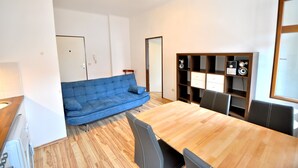 A modern living space with a wooden dining table, blue sofa, and built-in shelving with decorative items. - Apartment with one extra bedroom (Fürstenfeld)