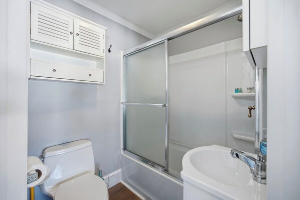 Un baño con inodoro, cabina de ducha de vidrio y lavamanos con espejo.