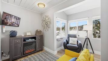 A modern living room with a fireplace, a sofa, a chair, and a large window offering a view of the outdoors.