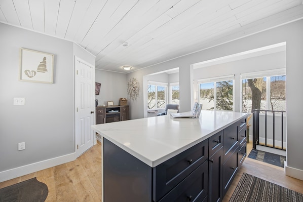 A modern kitchen with a large island, white walls, and a view of the outdoors.