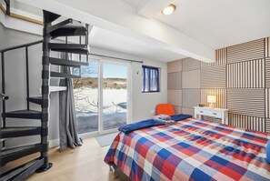 A bedroom with a bed, a desk, a chair, a window with a view, and a spiral staircase.