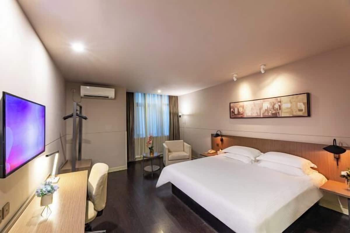 Habitación de hotel con una cama grande, un escritorio con silla, un televisor de pantalla plana, un equipo de aire acondicionado y un cuadro en la pared.