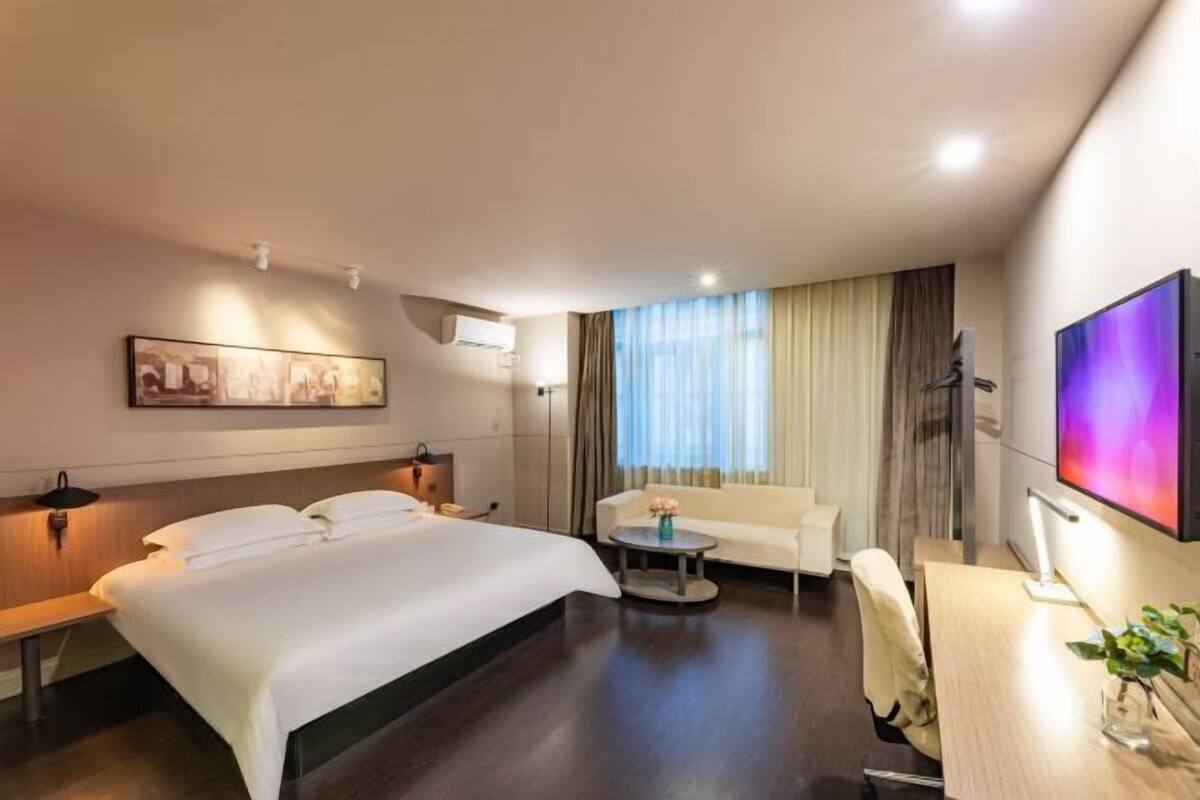 Habitación de hotel con una cama grande, un escritorio con una silla, una mesita redonda pequeña, un sofá, un televisor y un cuadro en la pared.