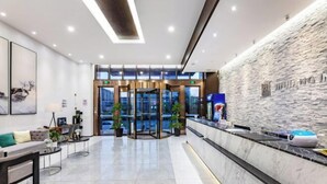 A modern hotel lobby with a reception desk, seating area, and a glass elevator.