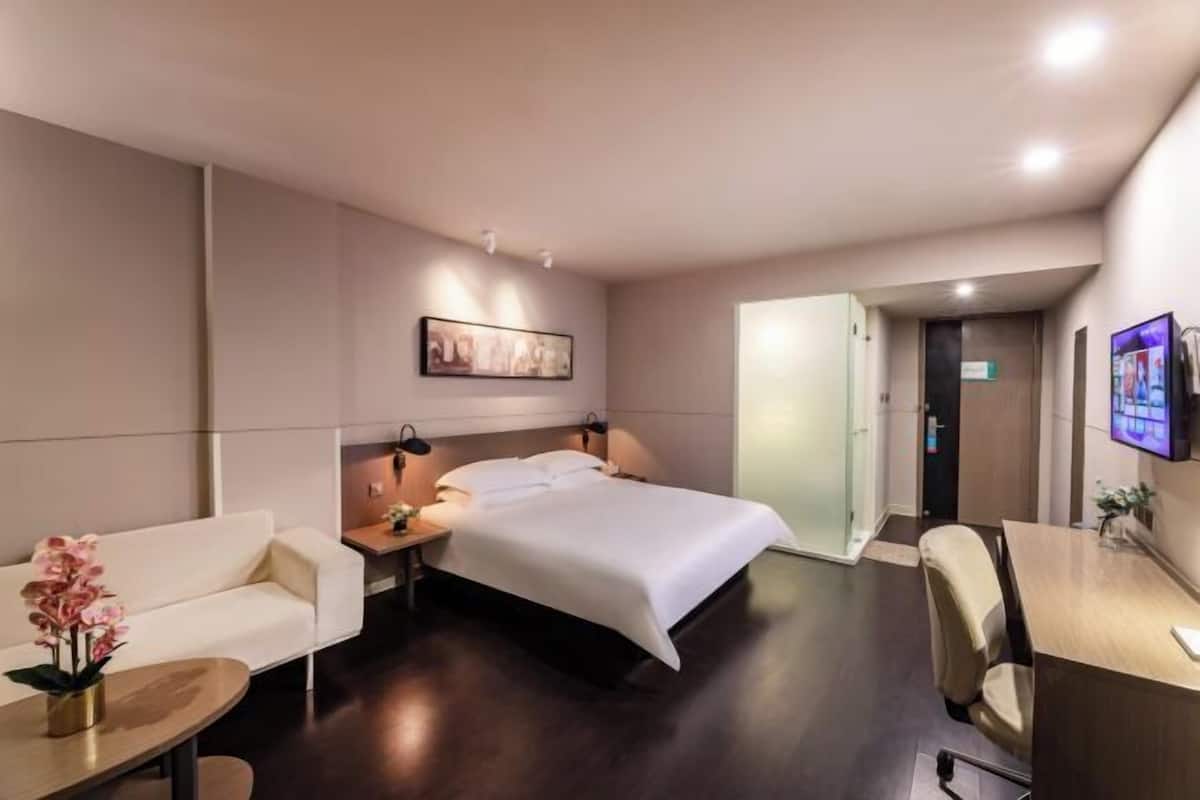 Habitación de hotel con cama, escritorio, silla, sofá, mesita de noche y televisor.