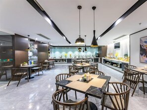 Un restaurante moderno con zona de comedor central, techo alto, iluminación colgante y una cocina visible al fondo.