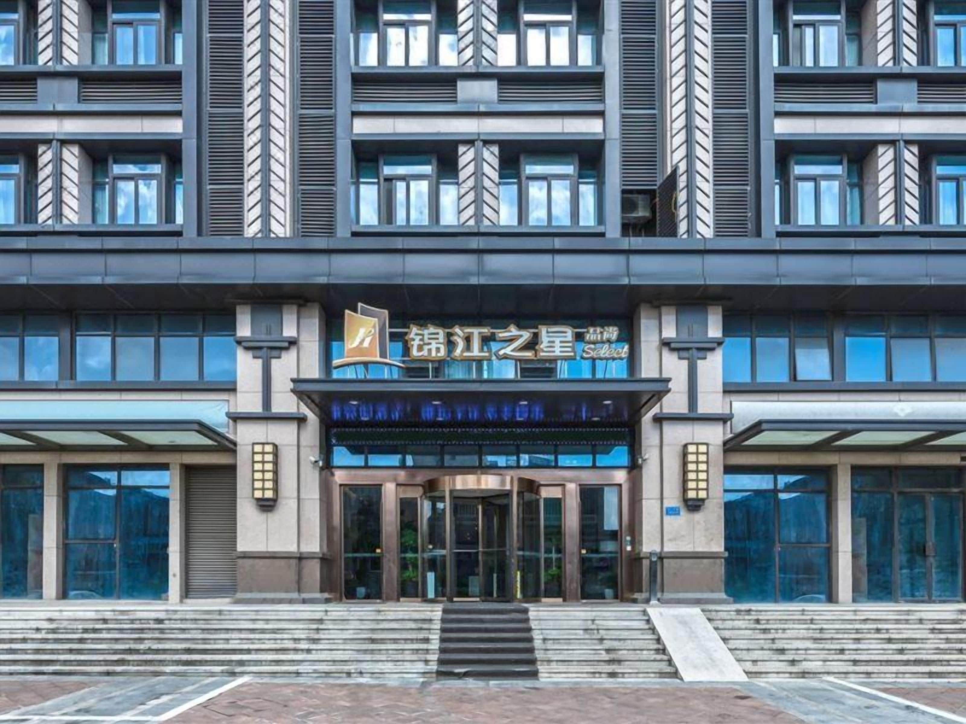 A modern building with a prominent entrance, large windows, and a sign indicating a hotel or accommodation.