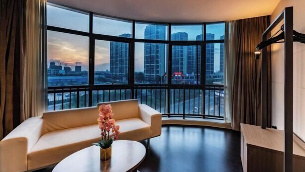 A modern hotel room with a curved balcony, a sofa, a coffee table, and a view of the cityscape.