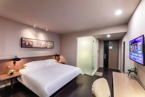 Habitación de hotel con cama, mesita de noche, cuadro en la pared, televisor y puerta que da a otra habitación.