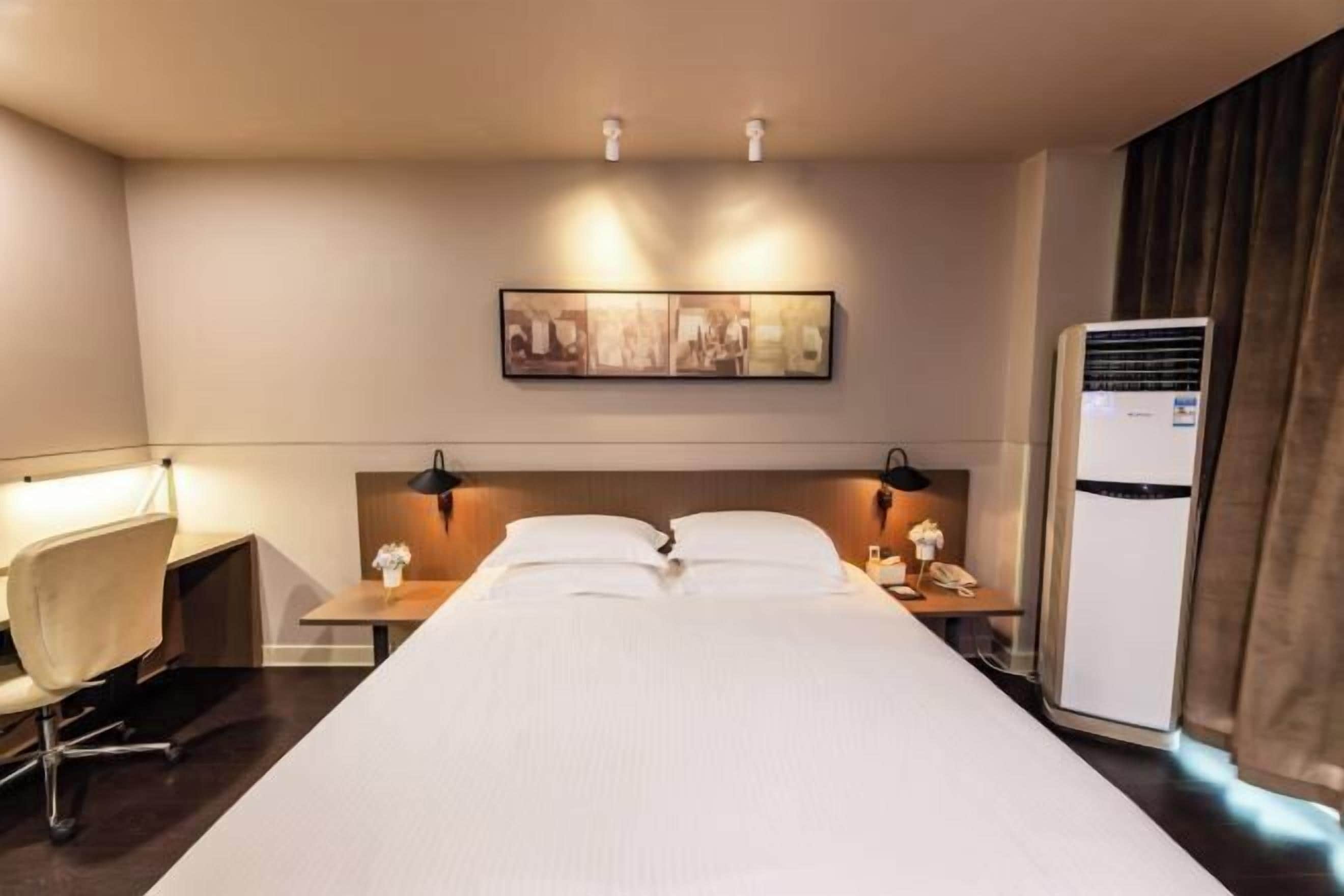 Et hotelværelse med en seng, to sengeborde, et skrivebord, en stol, en fastgjort aircondition og et billede i ramme på væggen.