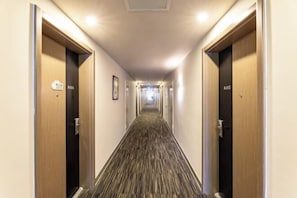 Un pasillo de hotel con puertas de madera, letreros de números de habitación y suelo alfombrado.