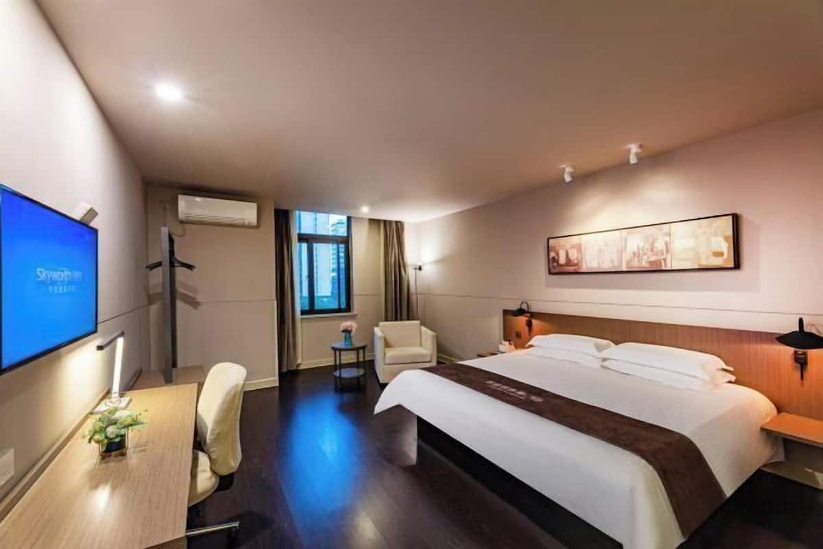 Una habitación de hotel con cama, escritorio, silla, televisor y ventana.