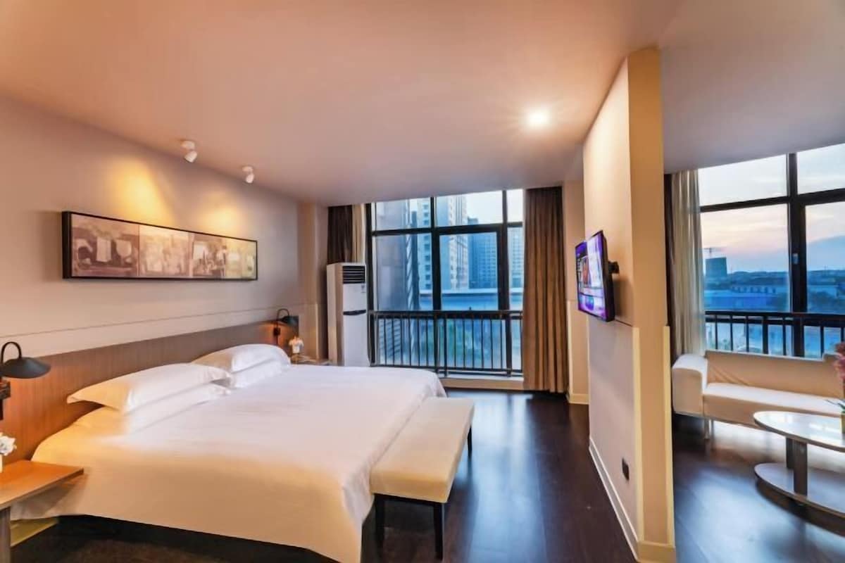 Habitación de hotel con una cama grande, un escritorio, una silla, un televisor y un balcón con vista a la ciudad.