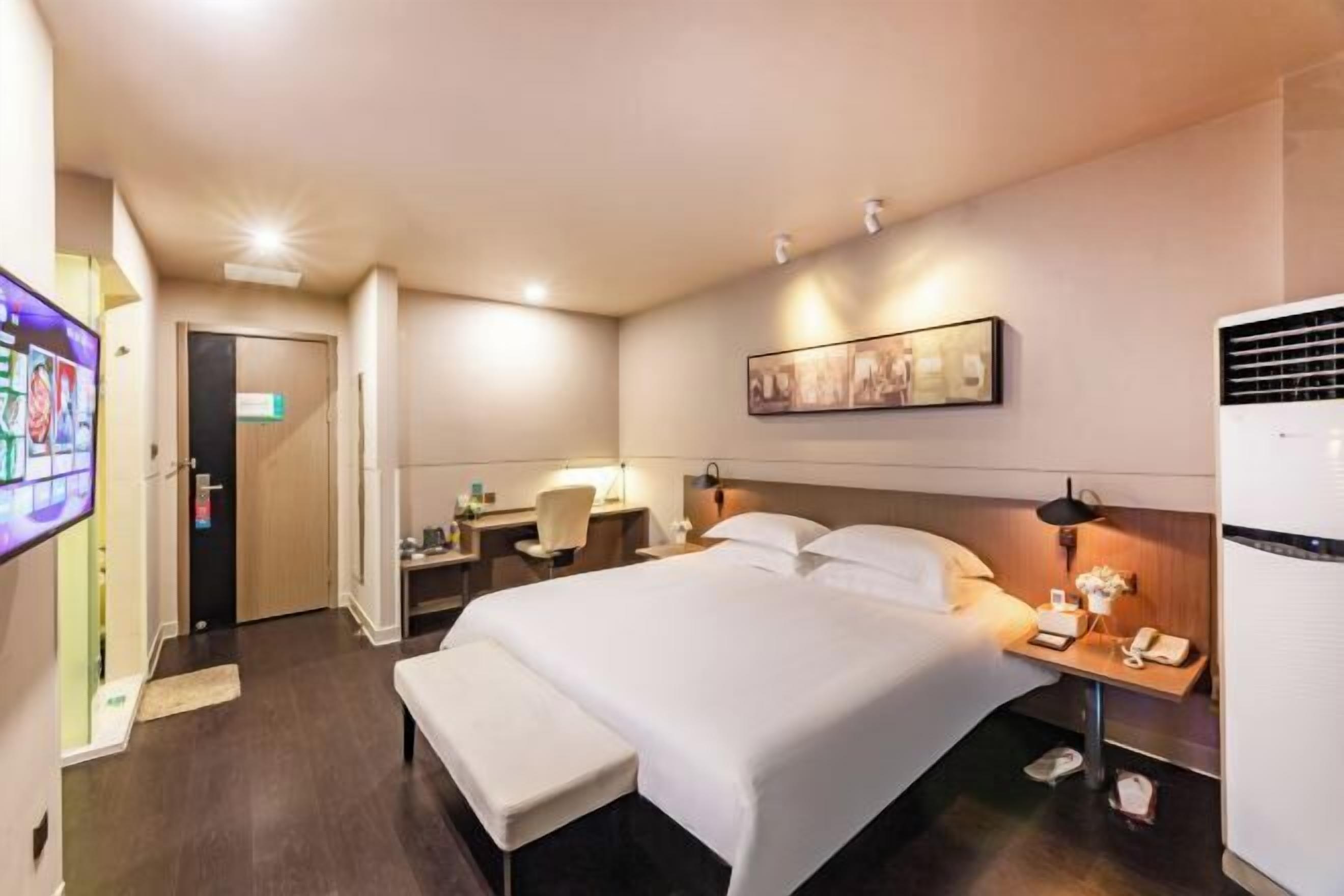 Habitación de hotel con cama, mesita de noche, lámpara y televisor instalado en la pared.