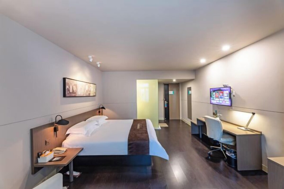 Una habitación de hotel con cama, escritorio, silla, televisor y una mesita.