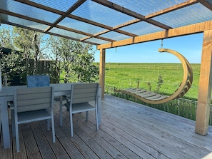 Un espace extĂ©rieur abritĂ©, dotĂ© dâun banc en bois, dâune table et offrant une vue sur un champ verdoyant.