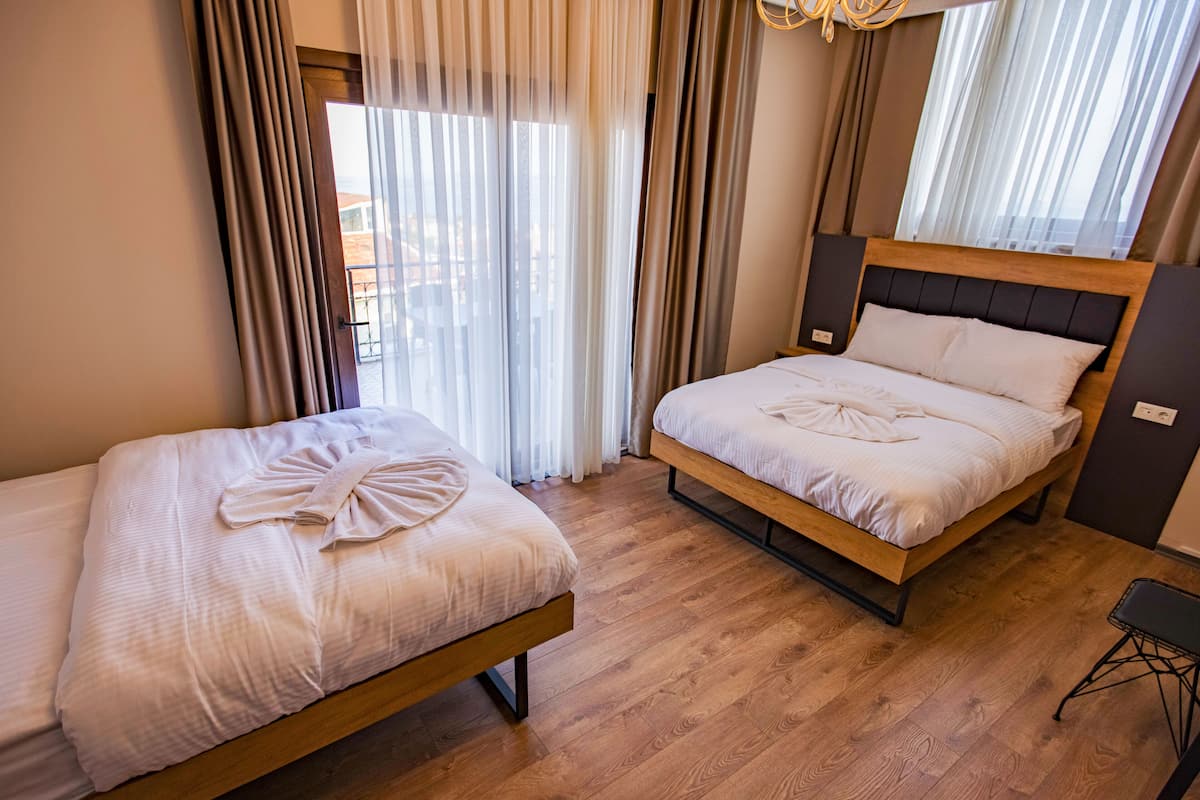 A hotel room with two beds, a wooden floor, and a view through sheer curtains.