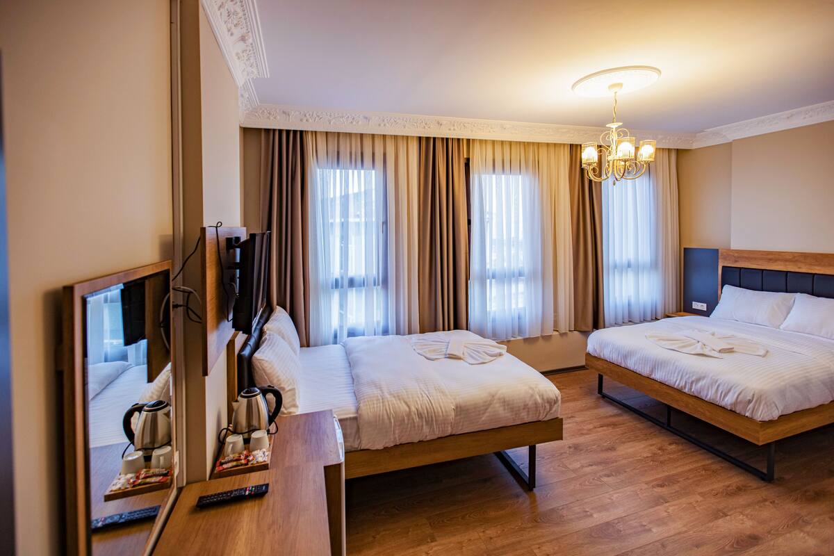A hotel room with two beds, a wooden floor, a chandelier, and a mirror reflecting the room.