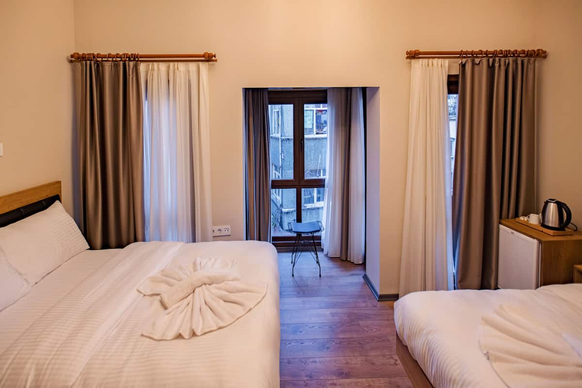 A hotel room with two beds, a small table, and a window with curtains.