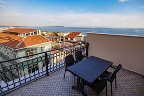 A balcony with a table and chairs, overlooking a coastal cityscape with buildings and the sea. - Grand Balyan Hotel & Restaurant (Istanbul)
