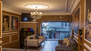 A spacious living room with a large sofa, a smaller armchair, and a chandelier. There is a television mounted on the wall and a balcony visible through an open door. - Grand Balyan Hotel & Restaurant (Istanbul)