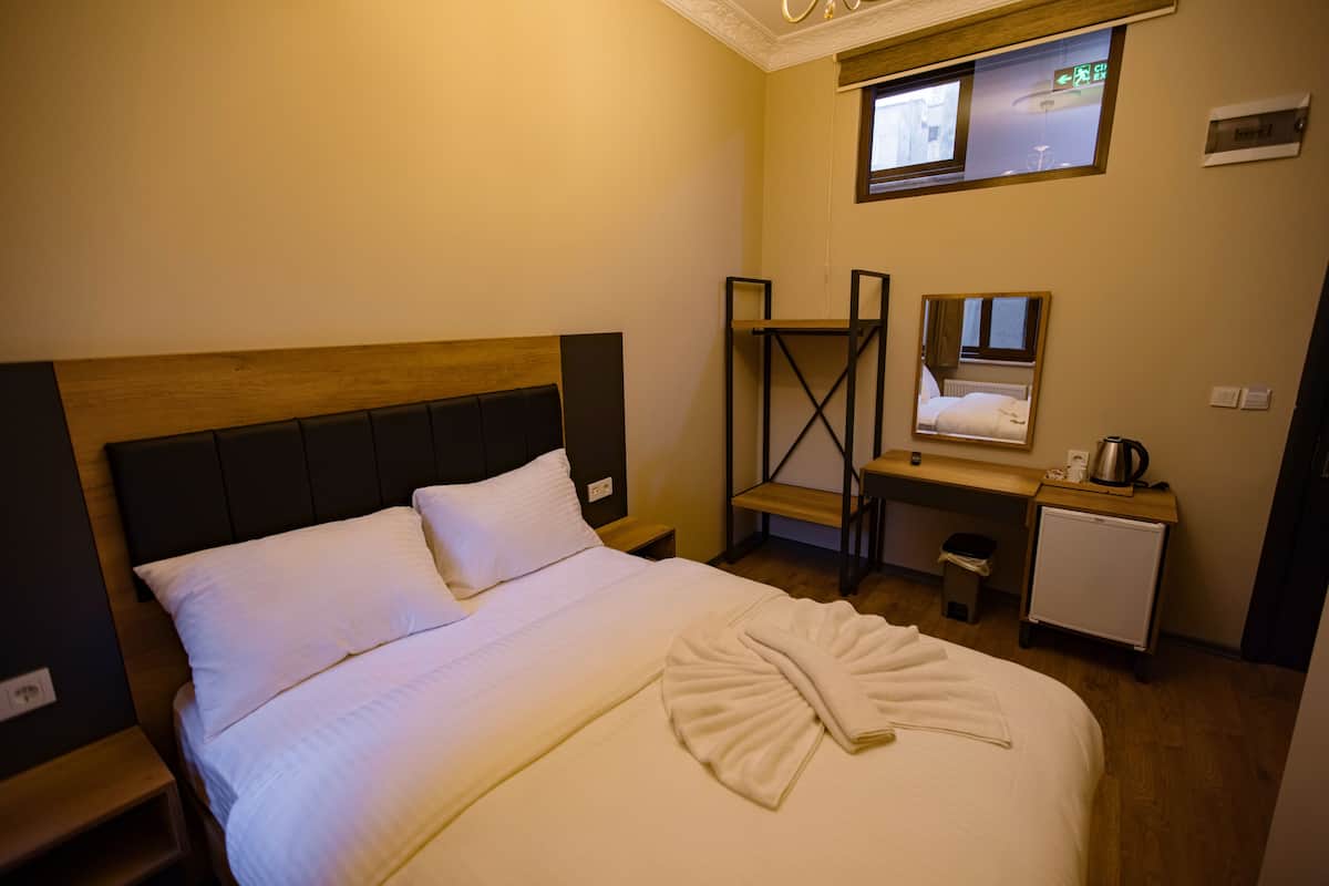 A hotel room with a bed, a small desk, a mirror, and a window.