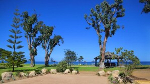 Un sentiero in legno conduce a un gazebo sul mare, circondato da grandi rocce e alberi.