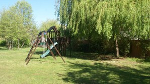 Un'area giochi con altalene e scivoli, circondata da alberi e prato.