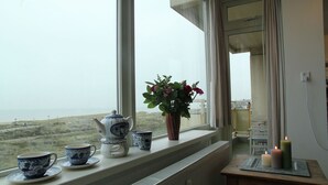 A view from a window with a table holding cups and a teapot, a potted plant, and candles. - Cosy apartment in Noordwijk aan Zee with balcony (Noordwijk aan Zee)