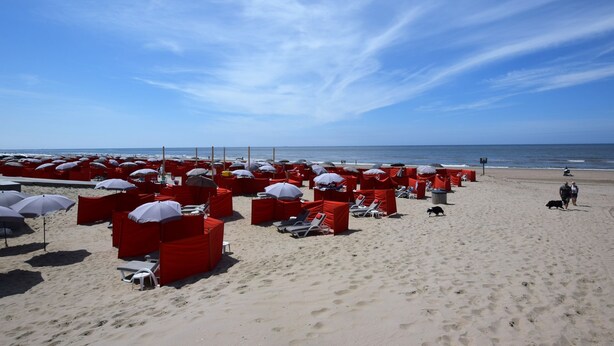 A beach with rows of red beach chairs and umbrellas, a sandy beach, and the ocean in the background. - Cosy apartment in Noordwijk aan Zee with balcony (Noordwijk aan Zee)