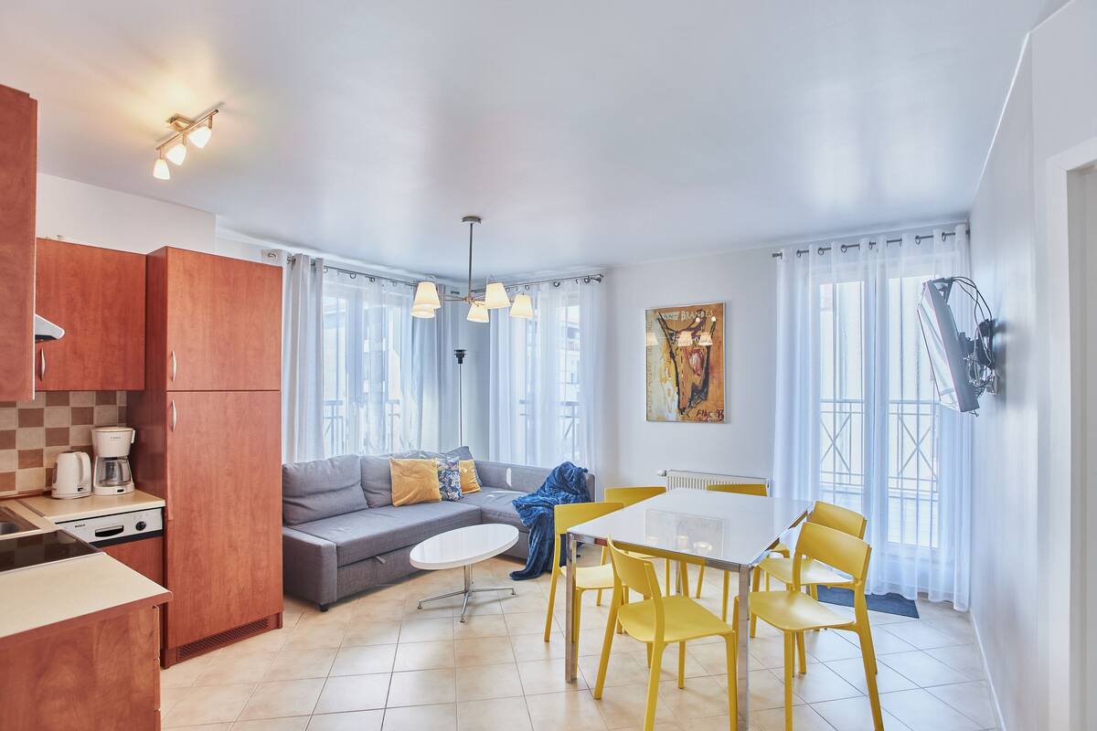 A modern kitchen with a dining area, a sofa, and a painting on the wall.
