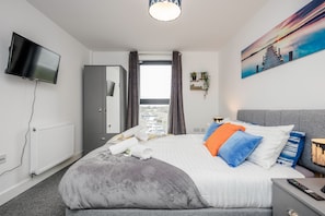 Moderni hotellihuone, jossa on suuri sänky, taulutelevisio, vaatekaappi, ikkuna verhoilla ja taulu seinällä.