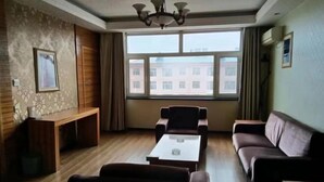 Uma sala de estar com sofá, poltronas, mesa de centro, um armário de madeira e uma janela grande com vista para edifícios.
