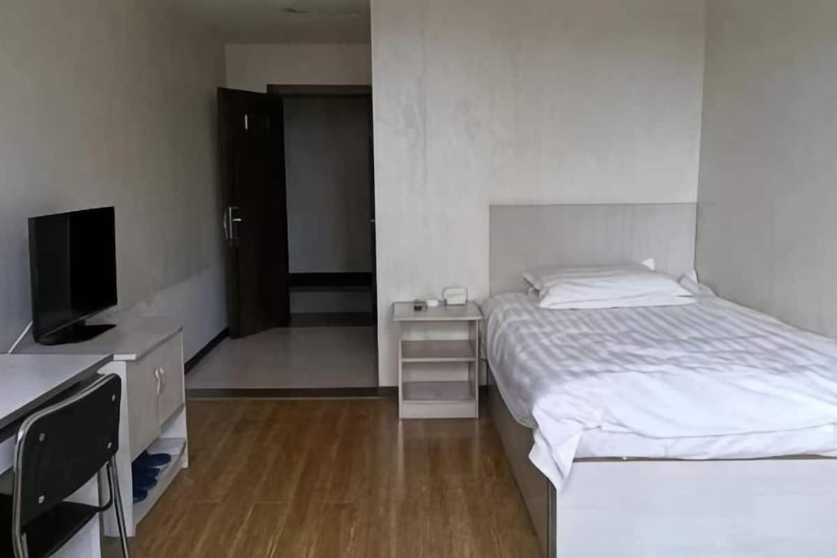 A hotel room with a bed, a desk with a chair, a television, and a door leading to another room.