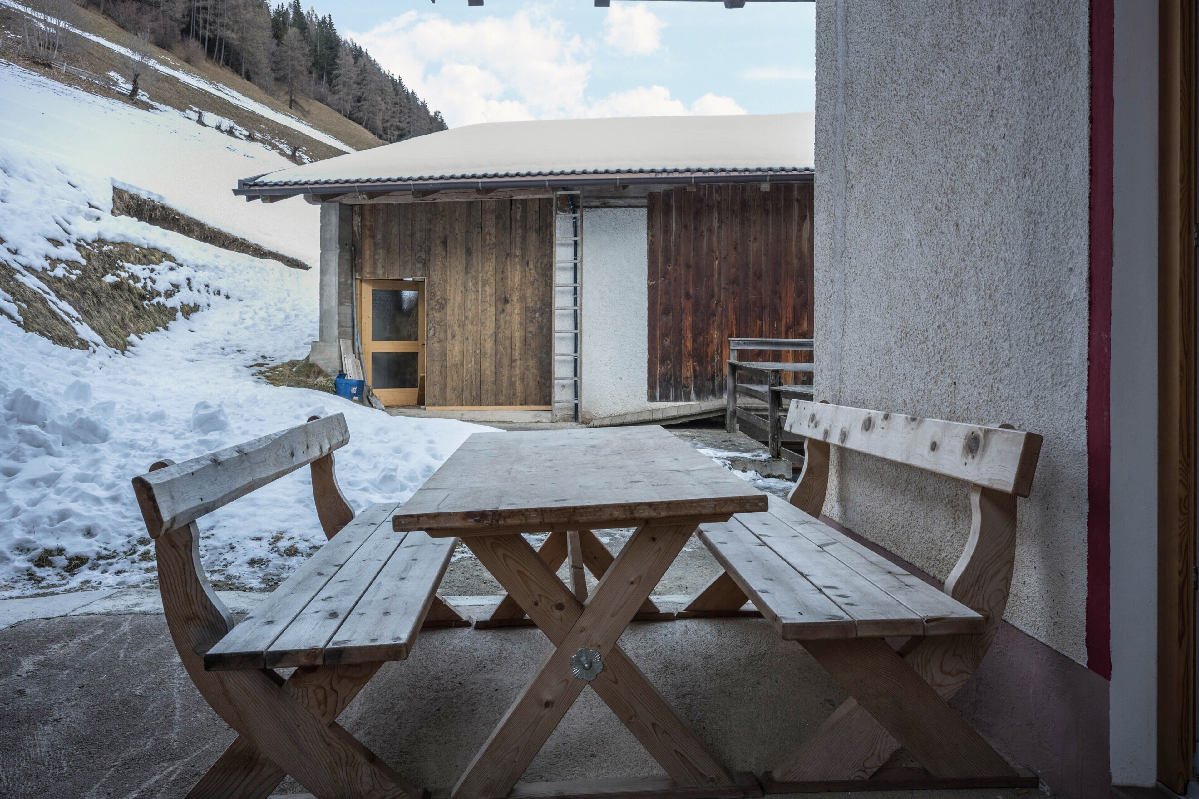 Ein Holztisch mit Bänken, ein Betonboden und ein Gebäude mit einer Holztür und einer Leiter.
