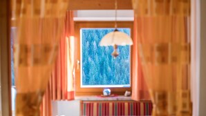 Habitació amb finestra, cortines, una làmpada penjant i una prestatgeria.