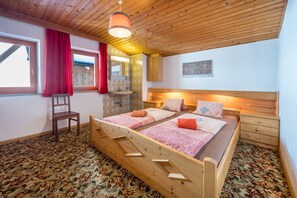 A wooden bed with two pillows, a nightstand, a chair, and a window with a red curtain.