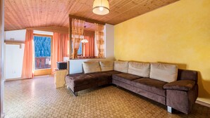 Habitació amb sostre de fusta, un sofà marró, una paret groga i una finestra amb cortines.
