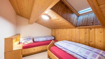 Ein kleiner Raum mit Holzboden und -wänden, zwei Betten, einem Oberlicht und einer geneigten Decke.