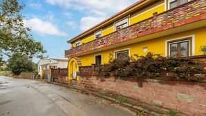 Un bâtiment jaune avec un mur en briques, un balcon et une porte surmontée d’une arche jaune.