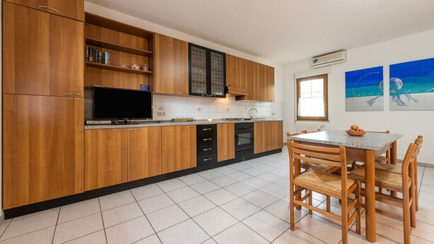 Une cuisine moderne avec des meubles en bois, un four encastré, une table à manger avec des chaises et des œuvres d’art accrochées au mur.