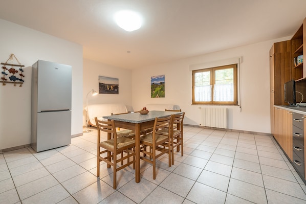A kitchen with a dining table, chairs, a refrigerator, a window, and a wall-mounted picture.