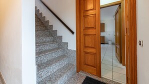 Un escalier menant à une porte en bois, un sol carrelé et un aperçu d’une cuisine.