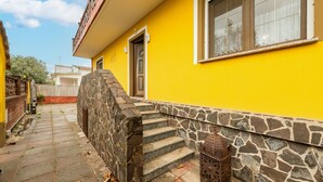 A yellow building with a stone staircase leading to a door, a window with a view, and a metal lantern on the ground. - Apartment Casa Colonia 1 with Sea View, Shared BBQ and Wi-Fi (Sant'Anna Arresi)