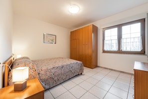 Une chambre à coucher comprenant un lit, une table de chevet, une lampe, une armoire et une fenêtre avec des rideaux.