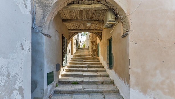 Una stretta scala in pietra conduce a una porta incorniciata da un arco, con soffitto e pareti rustici.